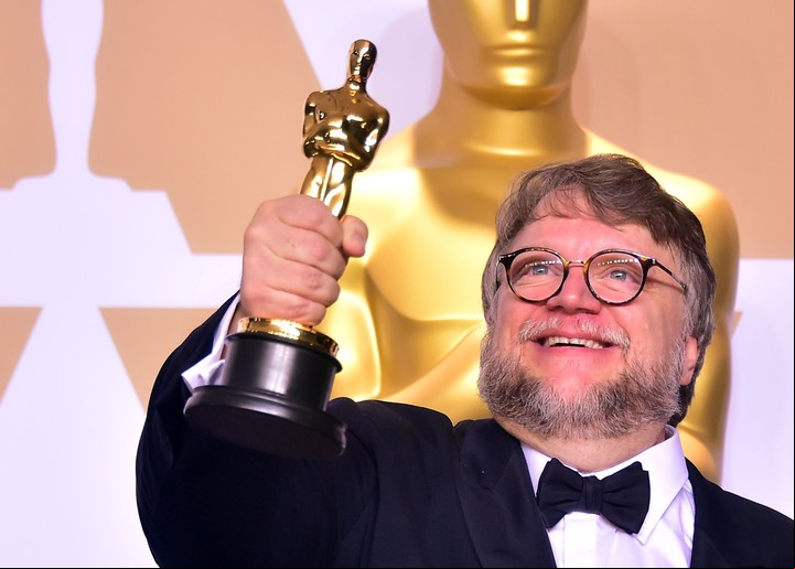 Sonriente, el director Guillermo del Toro levanta su estatuilla.