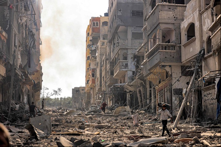 Un hombre lleva una garrafa de gas propano a la espalda mientras camina entre los escombros y la destrucción que ensucian una calle del campo de refugiados palestinos de Jabalia, en la ciudad de Gaza, el 11 de octubre de 2023, en el quinto día de combates entre el movimiento islamista palestino Hamás e Israel. (Foto de MAHMUD HAMS / AFP)