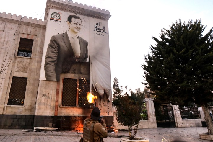 Un combatiente antigubernamental sirio dispara contra una gran pancarta con la imagen del presidente sirio, Bashar al-Assad, que cuelga de la fachada de un edificio municipal en la ciudad de Hama, en el centro-oeste del país, el 5 de diciembre de 2024. - Los rebeldes islamistas capturaron la ciudad de Hama, en el centro de Siria, el 5 de diciembre, días después de tomar Alepo, el centro comercial del país, en una ofensiva relámpago contra las fuerzas del presidente Bashar al-Assad. (Foto de Bakr ALKASEM / AFP)