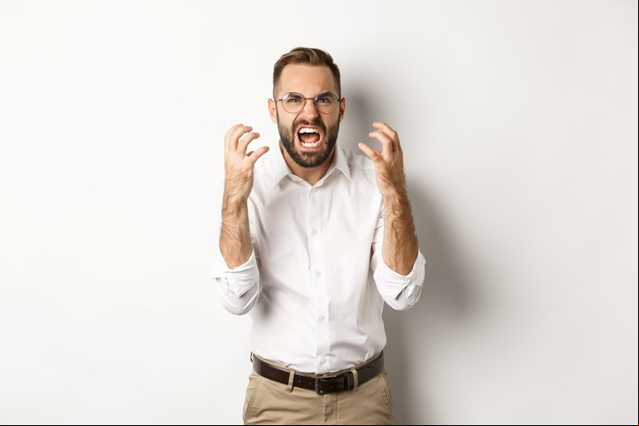 Frustrated and angry man screaming in rage, shaking hands furious, standing over white background.