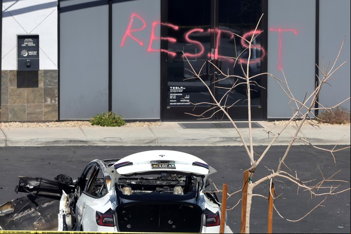 Un auto Tesla incendiado. De fondo un grafiti reza "Resistan". Foto: AP